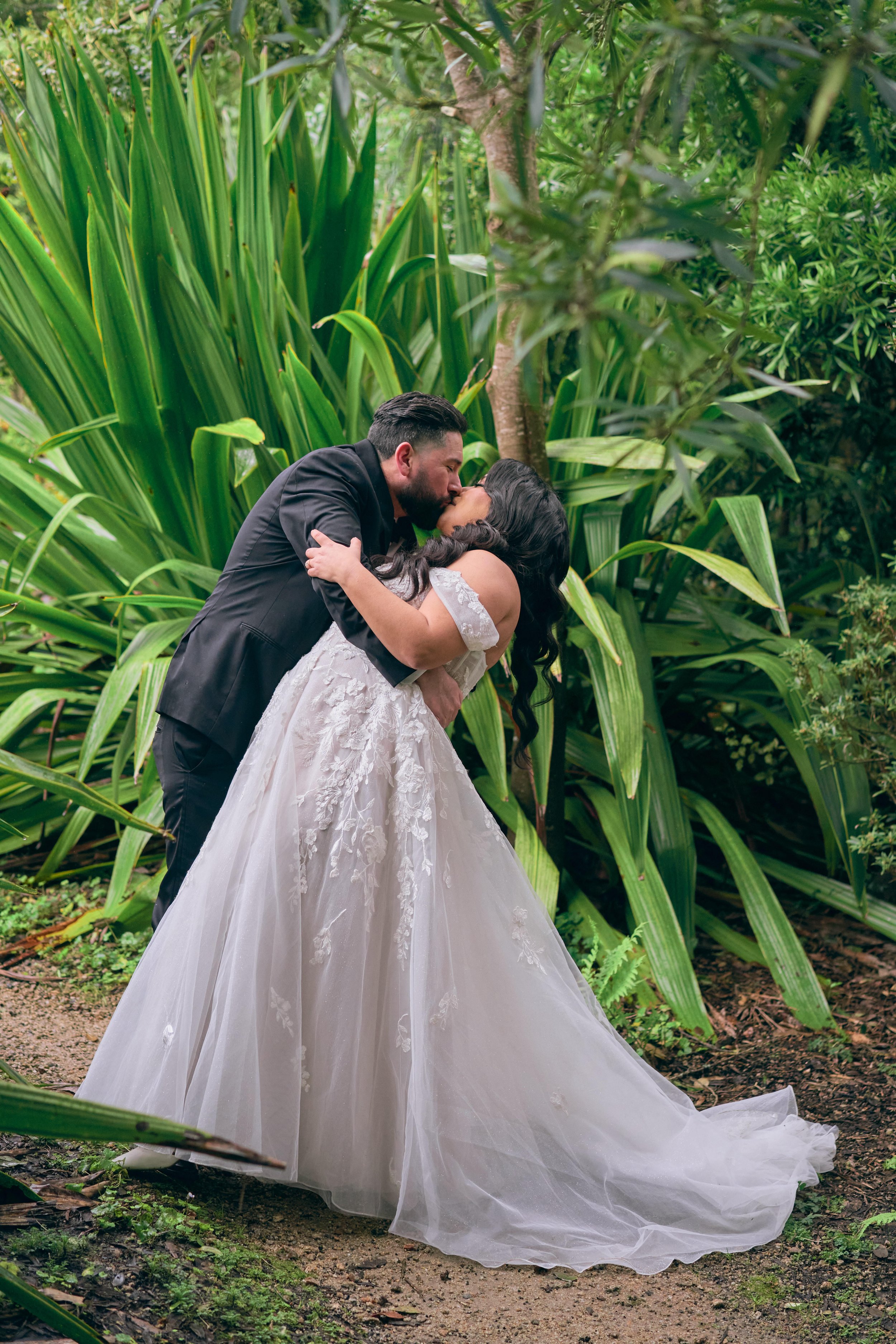 Groom embraces bride for a kiss amidst the greenery at San Francisco Botanical Gardens